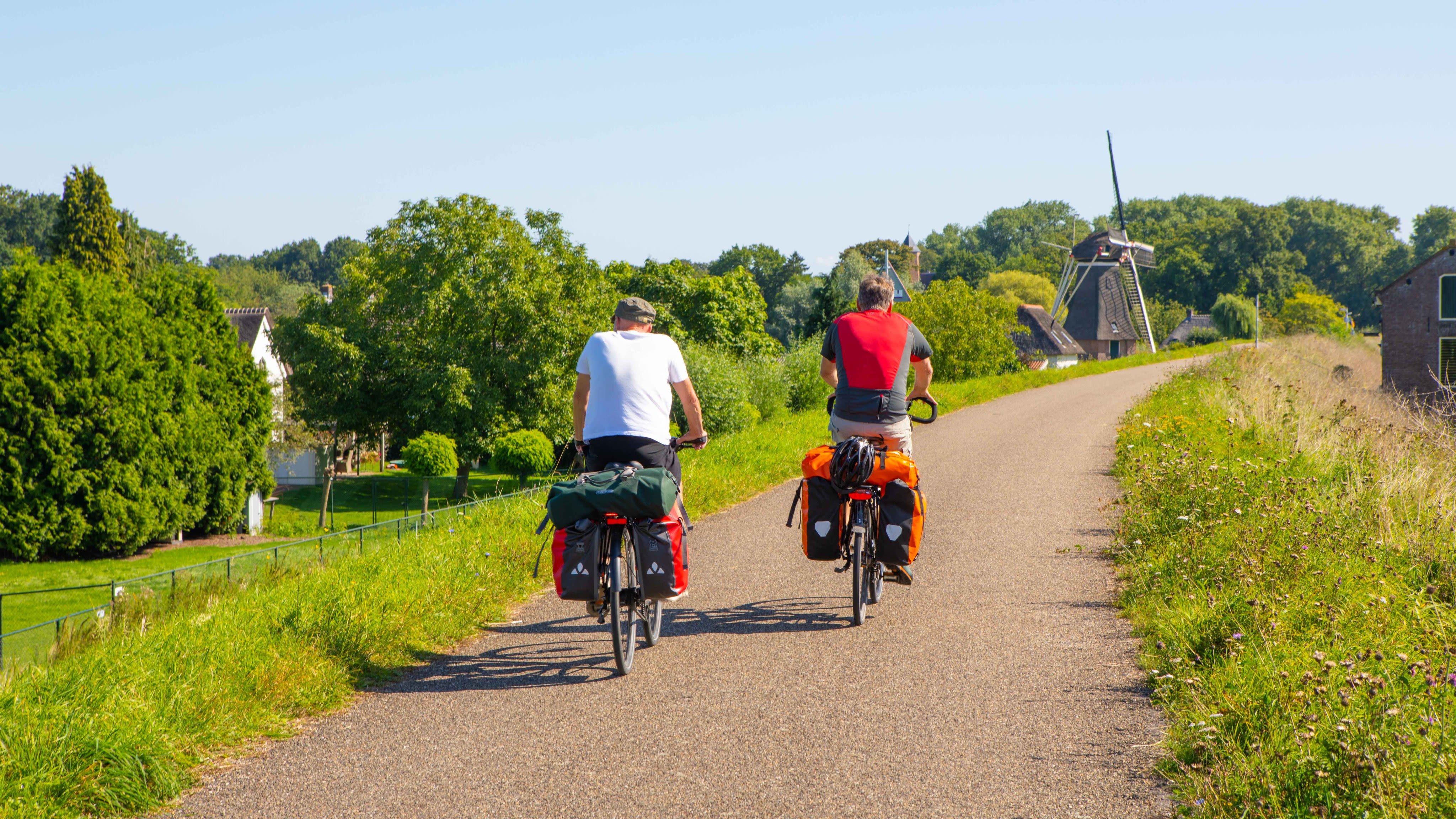 Twee fietsers op dijk met molen op de achtergrond tijdens zonnig en warm nazomerweer