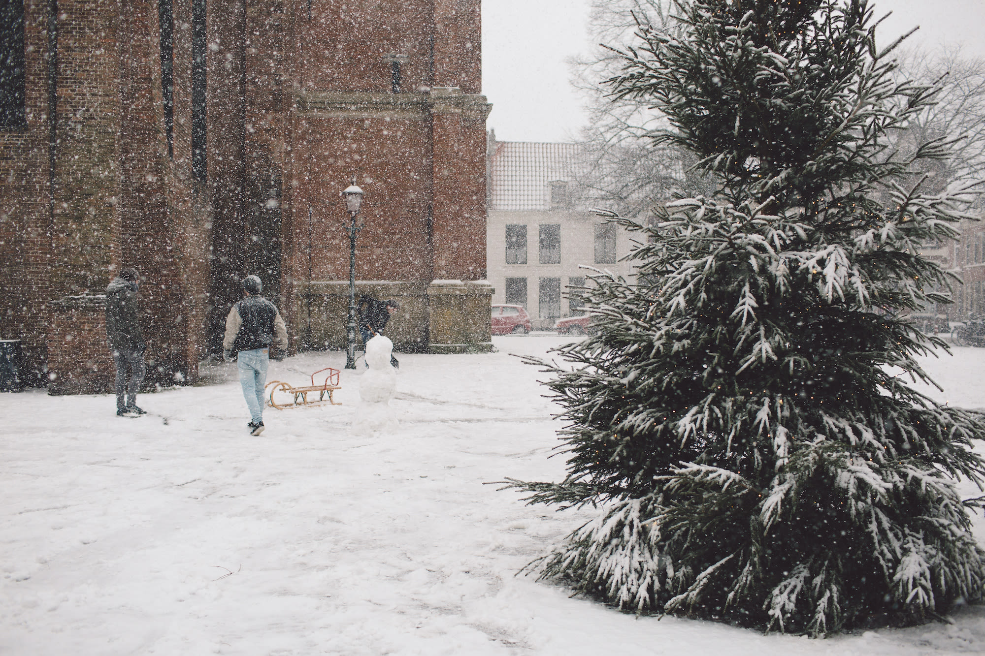 Sneeuwval met kerstboom en mensen met slee en sneeuwpop plezier op achtergrond