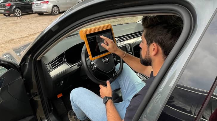 Hombre dentro de un coche usando una tablet de diagnóstico conectada al vehículo. Hombre dentro de un coche usando una tablet de diagnóstico conectada al vehículo.