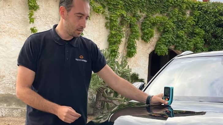 Hombre usando un medidor de espesor de pintura en el capó de un coche para comprobar reparaciones previas. Hombre usando un medidor de espesor de pintura en el capó de un coche para comprobar reparaciones previas.