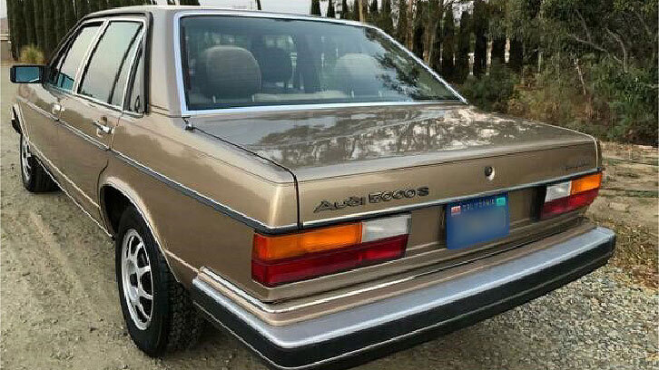 Heckansicht eines beigen Audi 5000S Oldtimers auf einem Feldweg. Heckansicht eines beigen Audi 5000S Oldtimers auf einem Feldweg.