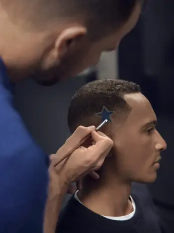 Fryzjer maluje niebieską gwiazdkę na boku głowy mężczyzny.