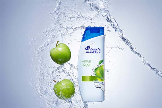 Dwa zielone jabłka i woda odbijają się od butelki  szamponu Head&Shoulders.