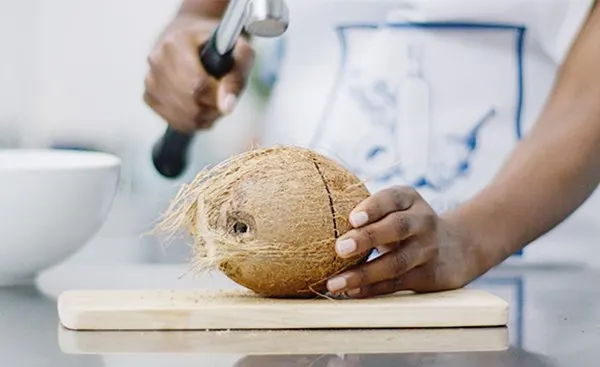 Kobieta rozbija na pół kokos młotkiem.
