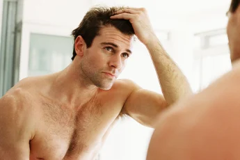 Mężczyzna ogląda swoje włosy i skórę głowy w lustrze.