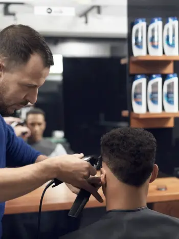 Fryzjer za pomocą trymera tworzy fryzurę mężczyźnie.