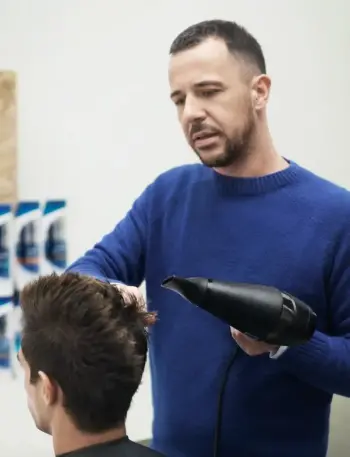 Fryzjer układa włosy klientami za pomocą suszarki.