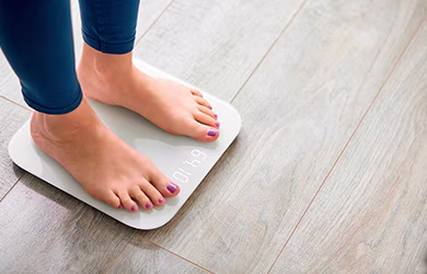 Close-up of a woman's bare feet with purple nail polish standing on a white digital weighing scale.