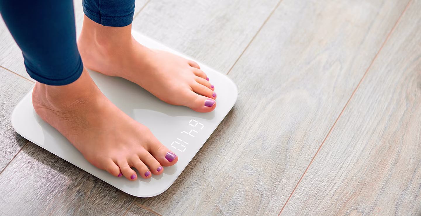 Close-up of a woman's bare feet with purple nail polish standing on a white digital weighing scale.