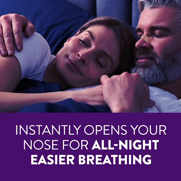 Two people lying on navy blue sheets in bed, one wearing a nasal strip, with the text "Instantly opens your nose for all-night easier breathing" on a purple background.