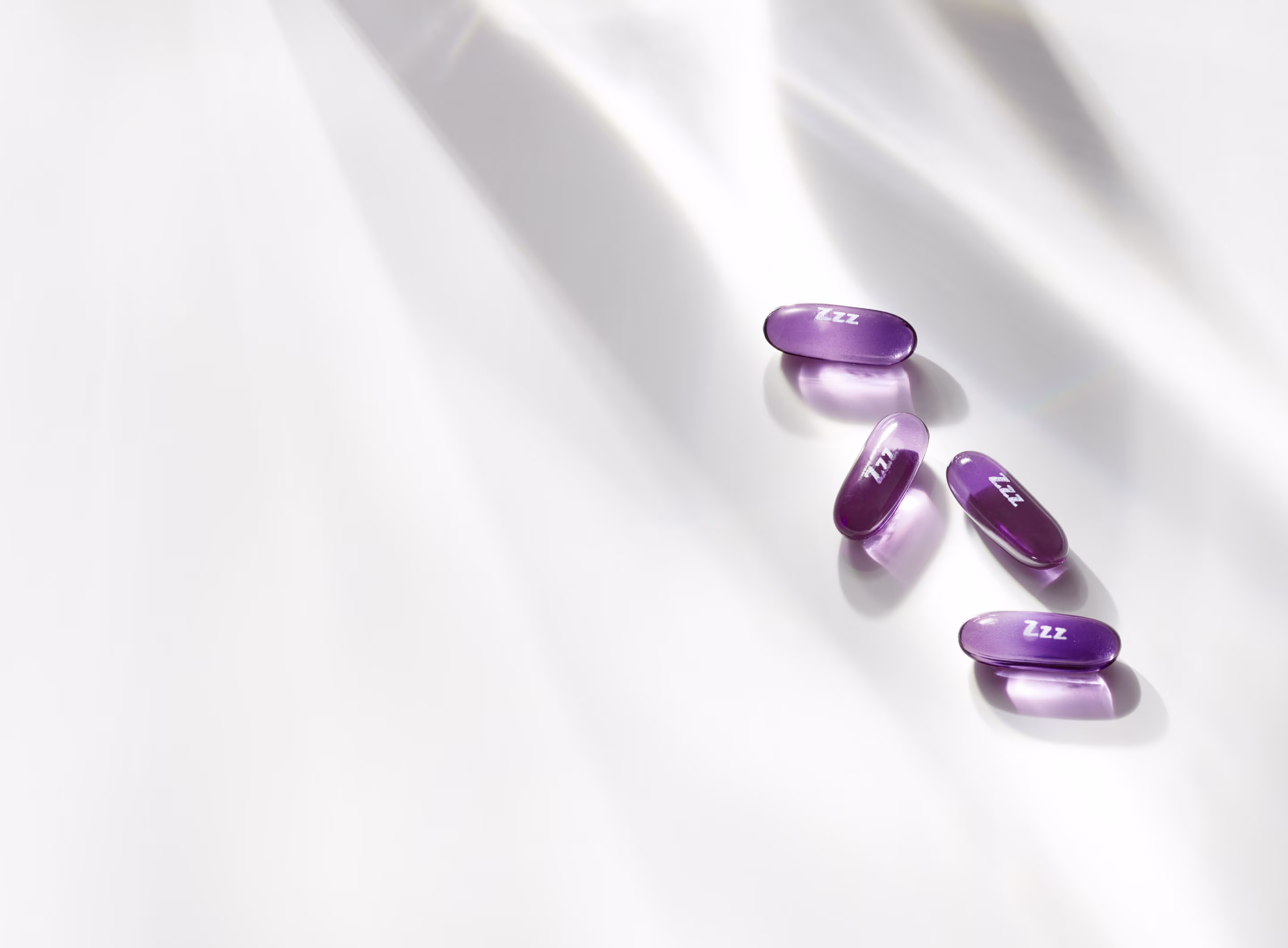 Four glossy purple ZzzQuil liquicaps on a white surface with soft shadows.