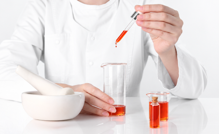 A laboratory specialist dispenses a red cosmetic oil sample into a glass beaker