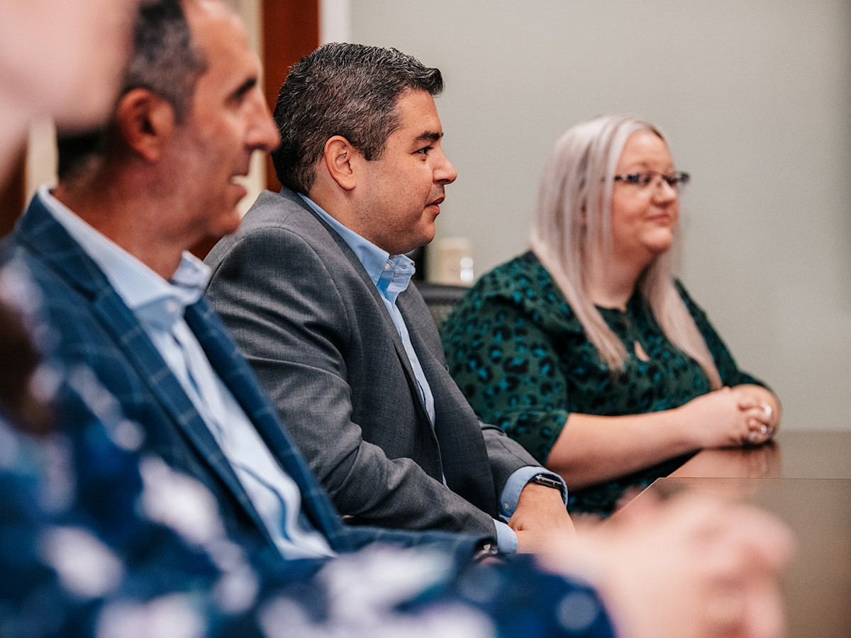 A photo of three CVG employees, two males and one female, sitting in line in a conference room.