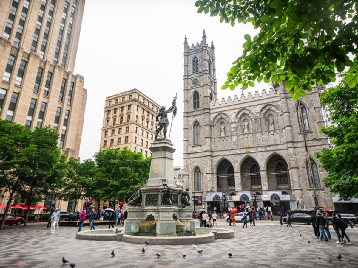 A photo of Montreal, Quebec, Canada that showcases a fountain and large buildings along a cobblestone street.