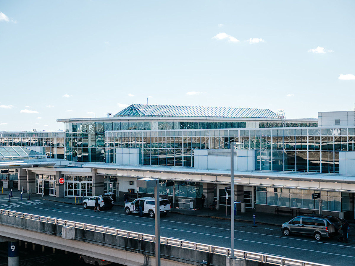 A photo of the glass exterior of CVG Airport on a bright day. There are cars driving in front of the airport.
