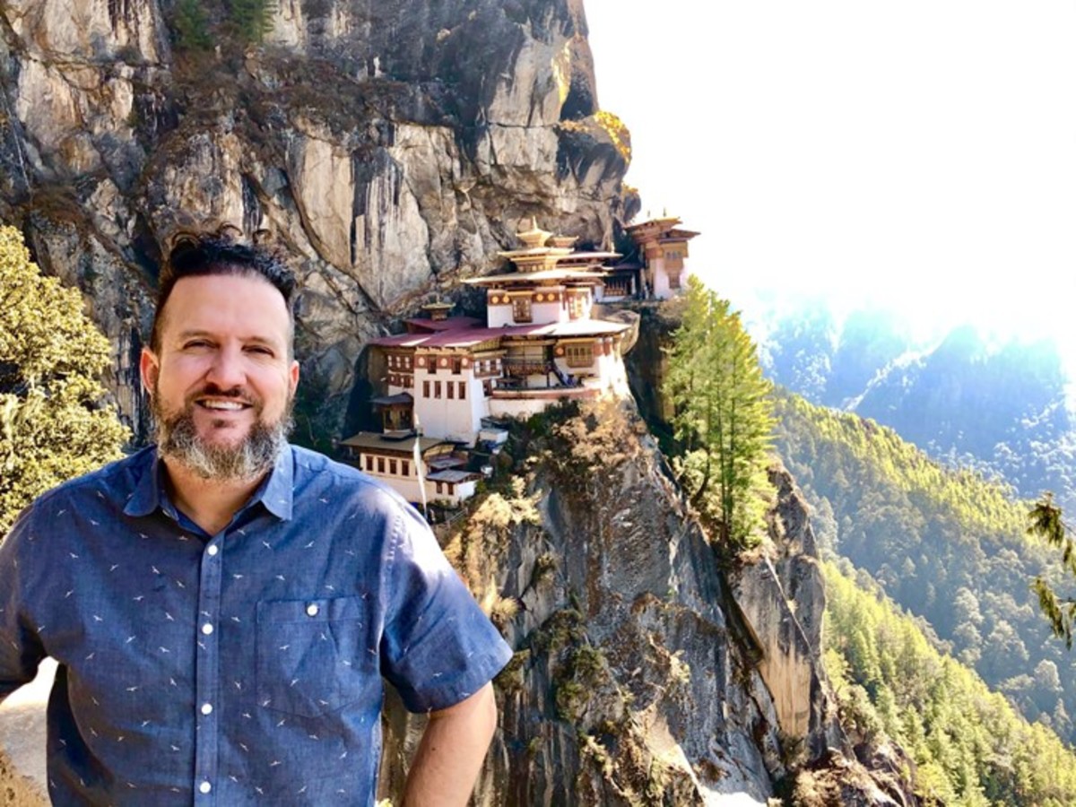 A photo of Randy Williams in Bhutan standing in front of buildings built on cliffs.