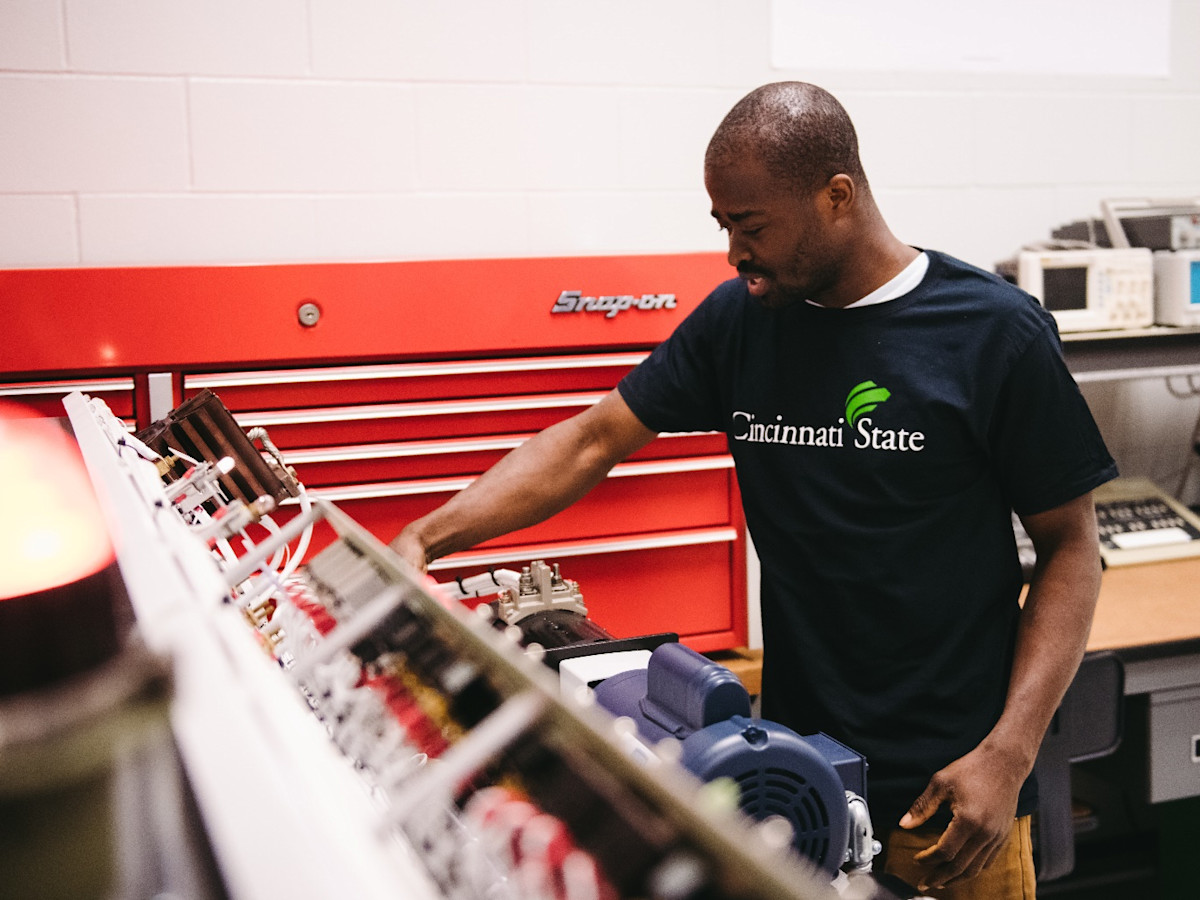 A photo of a man wearing a Cincinnati State t-shirt standing in front of a large red toolbox.