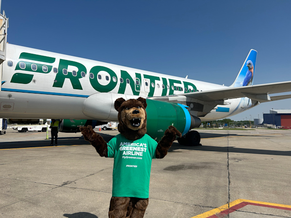 A photo of the Frontier mascot bear in front of a Frontier Airlines plane on the ramp.