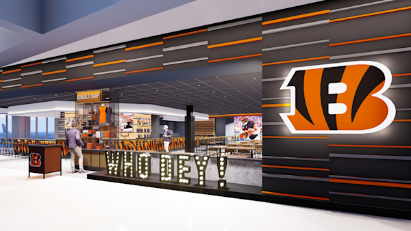 A photo of the Bengals Bar & Kitchen rendering. The walls are striped, grey, orange, and black. There is a light up Who Dey sign in front and a Bengals B on the front wall.