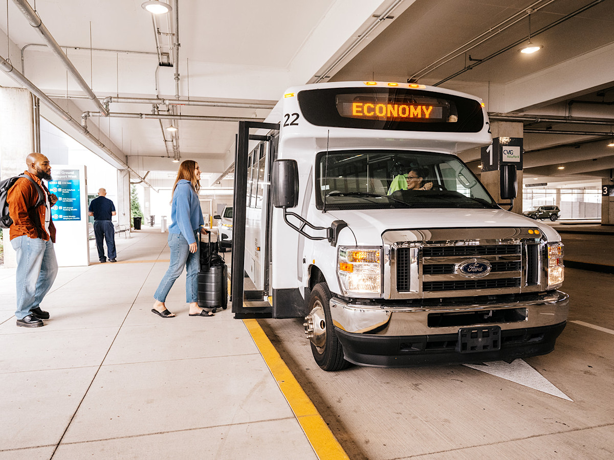 A photo of a white shuttle that says Economy on the digital sign on top is picking a male and female up in a parking garage structure.