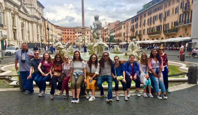 Students and professors sitting on the side of a fountain in Piazza Navona in Rome.