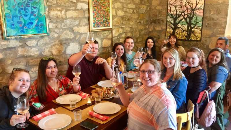 Several students and professors toasting to the camera in a Tuscan style restaurant in Tuscany, Italy.