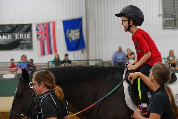a young boy riding a black horse wearing a red t-shirt