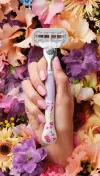 Female hand holding Venus Deluxe Smooth Sensitive + Rifle Paper Co. Razor with a lot of colorful flowers in the background