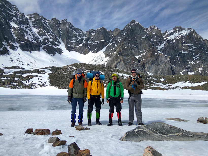 Four friends posing for a photo in the snow in front of a mountain and lake