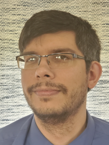 A headshot of Cody wearing blue on a tan patterned background.