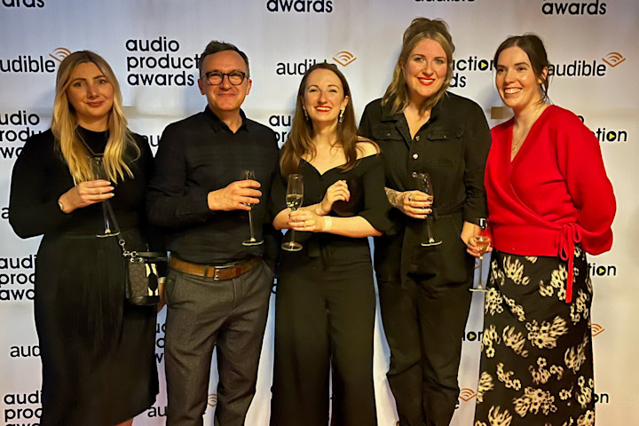 A group of five people are standing in front of a backdrop that says "Audio Production Awards"