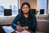 VP of Product Management Sue Shlapakovsky sits in Audible's office in Newark, NJ. She sits looking directly into the camera while wearing a teal sweater. A laptop computer sits open before her and a pad of paper which she is poised to write on.