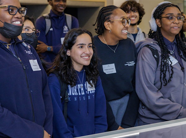 Group of interns smiling and wearing navy and grey uniforms.