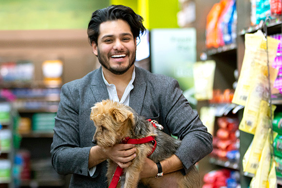 A man in a blazer carrying a small terrier with a red leash walks through a pet store in Newark.