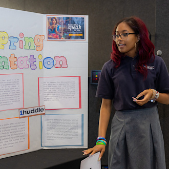 A student stands next to a large piece of posterboard presenting the information pasted on it.
