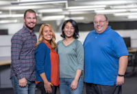 Four Audible Cambridge employees stand shoulder-to-shoulder looking straight at the camera smiling.