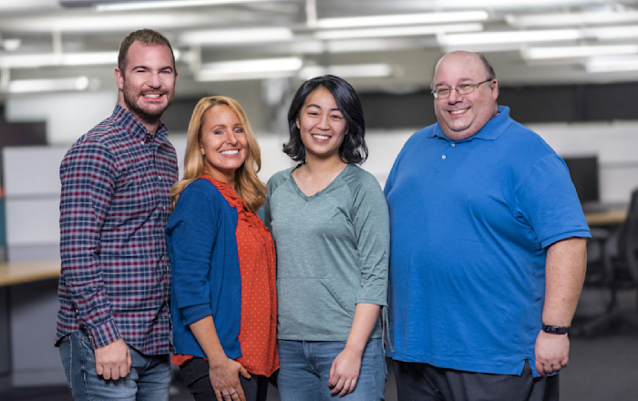 Four Audible Cambridge employees stand shoulder-to-shoulder looking straight at the camera smiling.