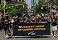 Members of the Audible community walk proudly in the 2022 New York City Pride Parade, holding a banner that says "Queer Stories by Queer Voices... Audible Pride" and holding rainbow-colored fans and flags.