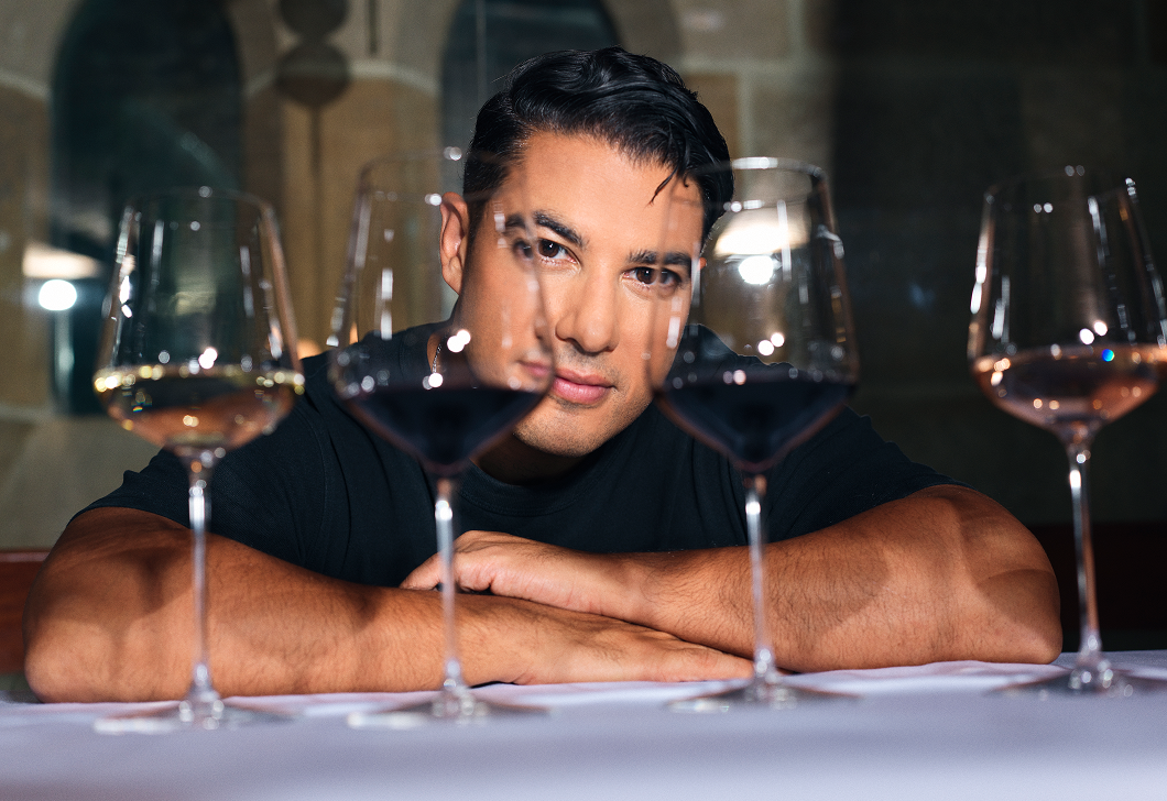 A photo of Marc Fennell, who's posed behind four glasses of wine.