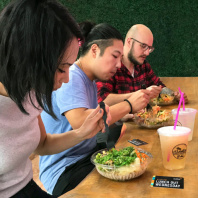 Three Audible employees sit at a lunch counter in a row eating their salads. A lunch out wednesday card sits by one of the employees' meals.