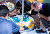 Several Audible employees and Newark artists paint leaves and other designs on the cement based of solar lights.