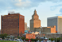 The Newark skyline appears at dusk as the light turns golden on the red brick buildings. The sky is blue with wisps of clouds. Two of Audible's office buildings appear in the foreground.