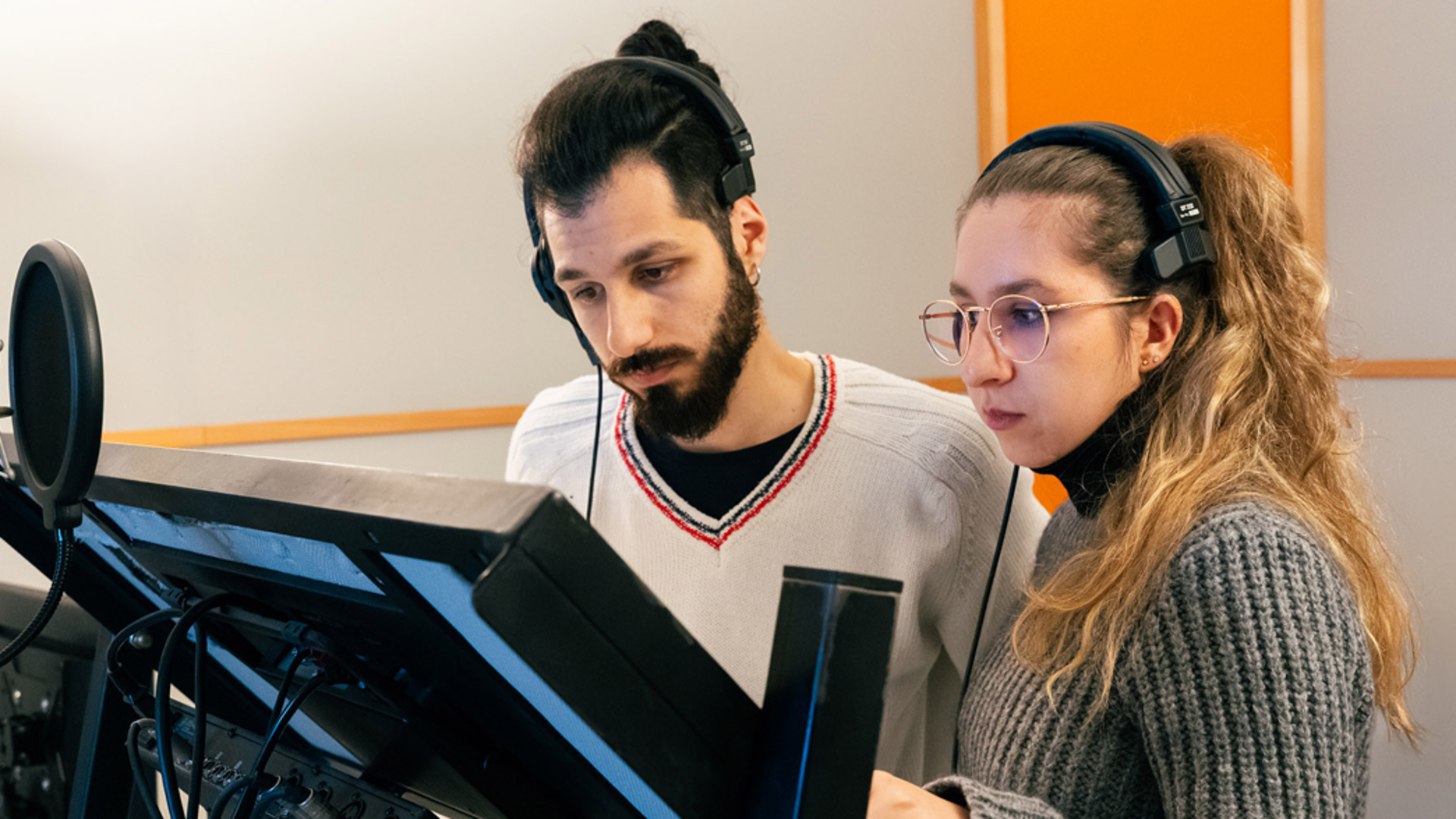 Two young actors stand with headphones on in front of a mic and stand holding a book they're narrating.