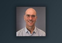 Tim Martin, Audible's CTO, is photographed against a neutral background. He is facing the camera and wearing glasses and a button down shirt.