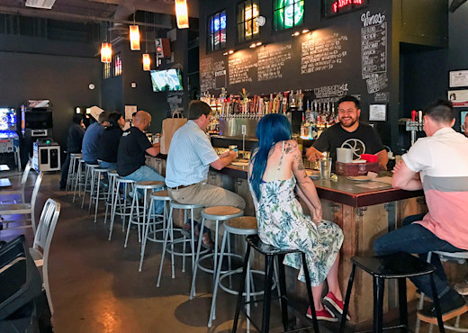 Several people sit at the bar of a restaurant with the bartender serving them from behind the counter.