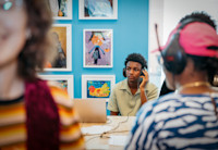 A teenager sitting at a desk, with a laptop in front of him. He's wearing headphones.
