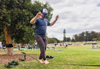 A man balances barefoot on a slack line strung between two trees in a park.