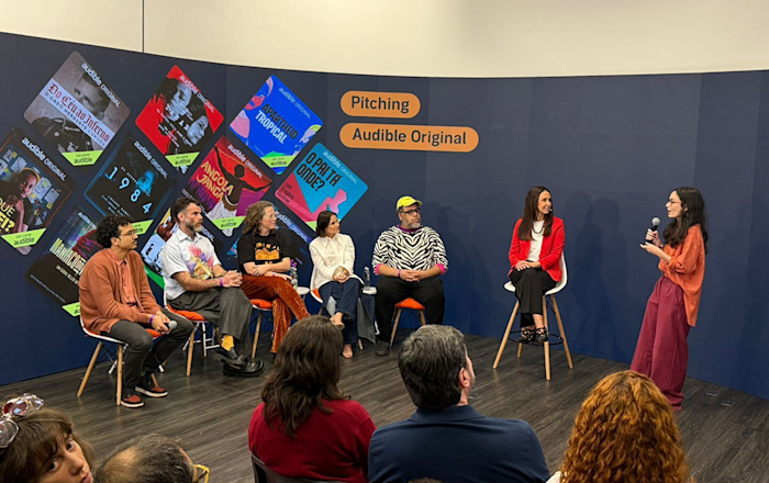 Mikaela Pasa apresenta o projeto vencedor do Pitching de sua equipe aos jurados Leo Neumann, Chico Felitti, Paula Scarpin, Bianca Comparato e MM Izidoro, sob o olhar de Adriana Alcântara, diretora-geral da Audible no Brasil.