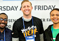 Three Audible employees stand in front of a while backdrop wearing Audible t-shirts.