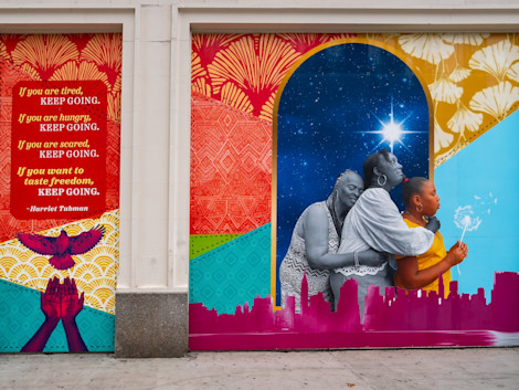 a mural on a school building depicting three generations of women, a North Star, and a bird flying out of hands